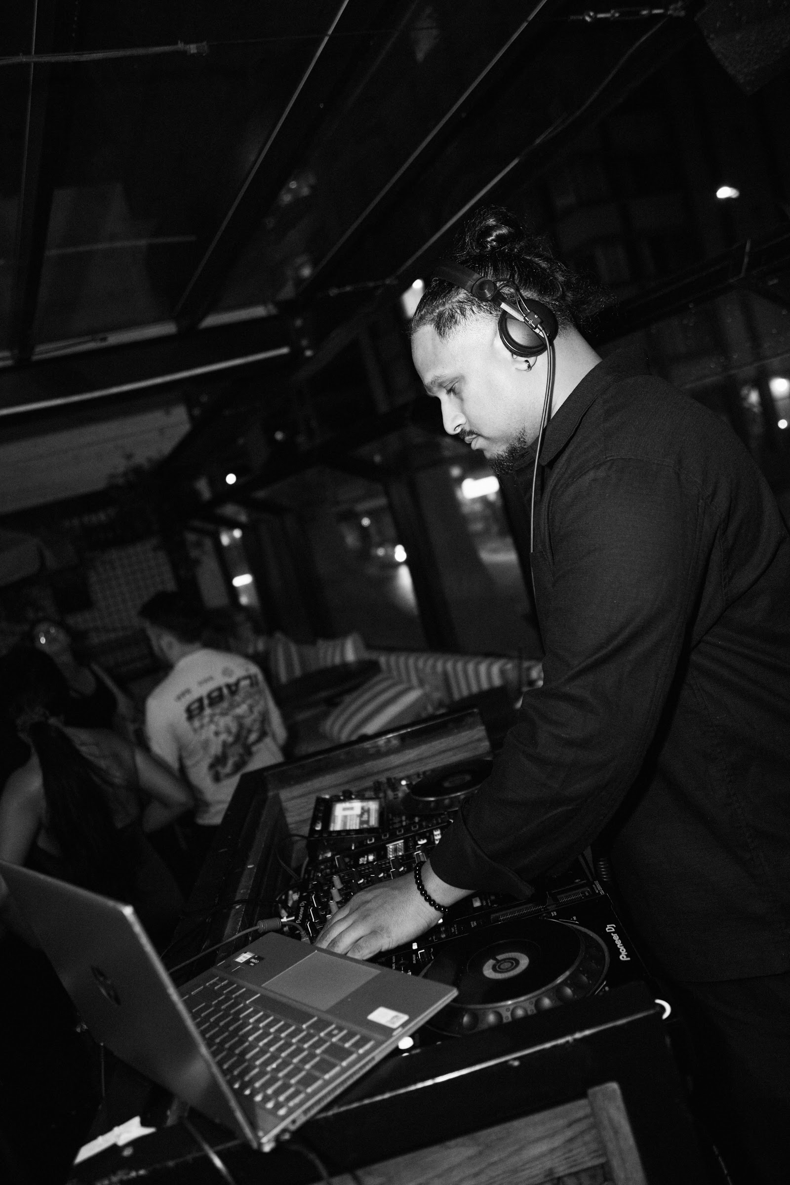 Black-and-white photograph of a DJ wearing headphones at the decks